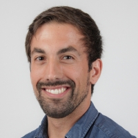 A smiling male face with short brown hair and short facial hair