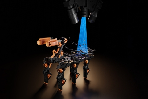 This rendering shows a robot being built layer-by-layer using the new process. The black spheres represent the material that the printer uses. The material is then cured by UV light, represented in blue. At the top of the image are the cameras that scan the procedure and adjust accordingly (Credits: Moritz Hocher).